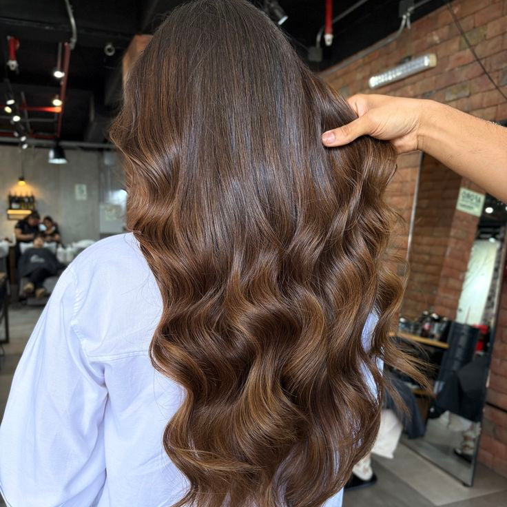 Person with long, wavy brown hair being styled in a salon.