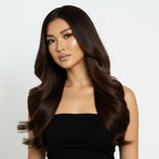 Woman with long, wavy brown hair wearing a black strapless top on a white background